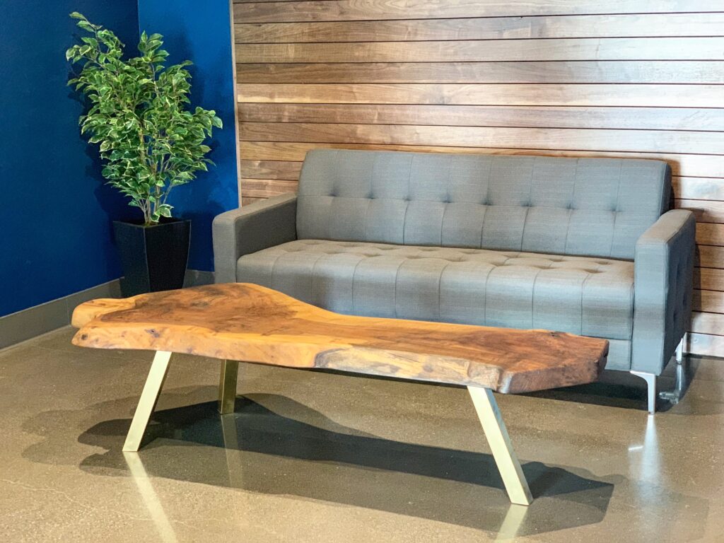 Live edge coffee table in Toronto with golden legs, placed in front of a grey sofa and wooden accent wall.