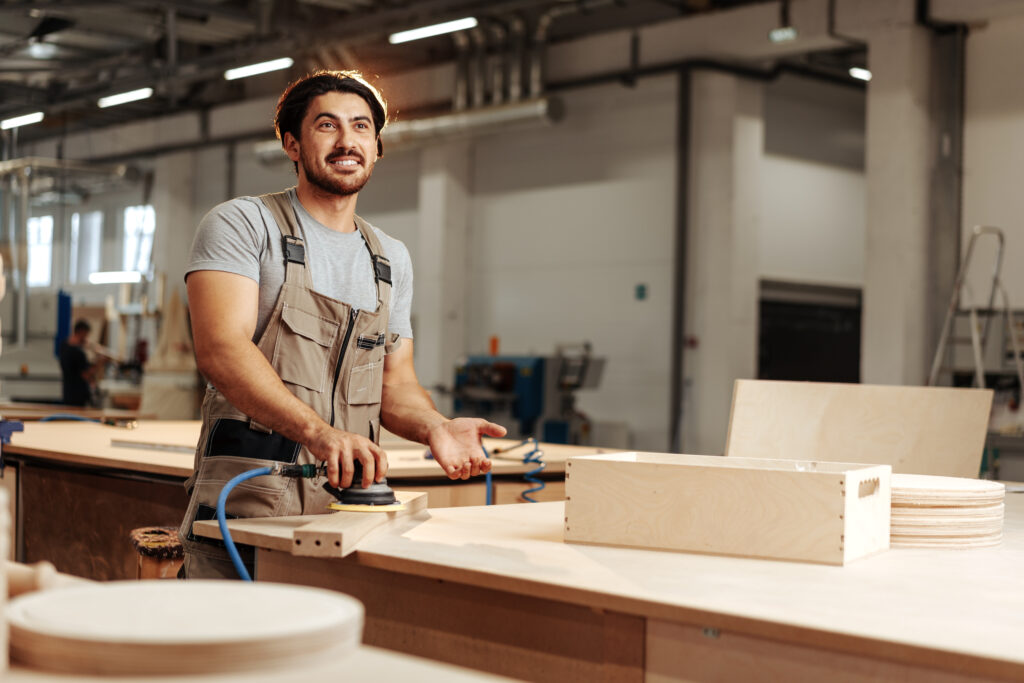 Smiling woodworker sanding wood in a modern Toronto workshop where live edge tables are crafted